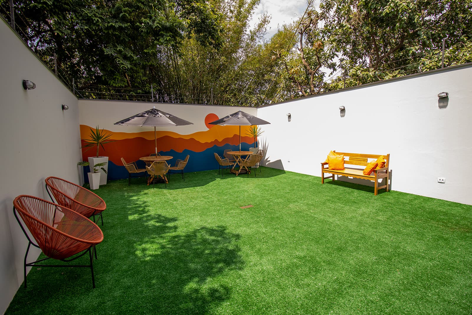 Foto real da área externa da Smart Hub, com o mural original do Sol ao fundo, gramado amplo e mobiliário nas laterais.